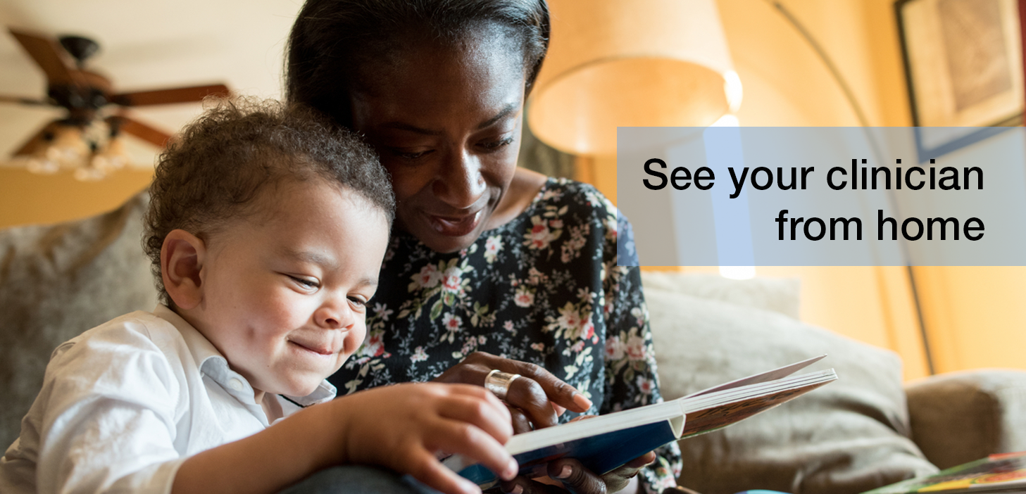 Black woman and child smiling, looking at book. They are sitting in a living room.